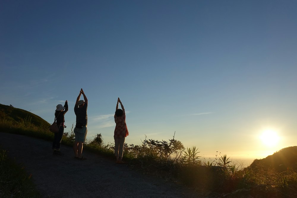 Trois amies saluent le soleil sur un chemin de colline